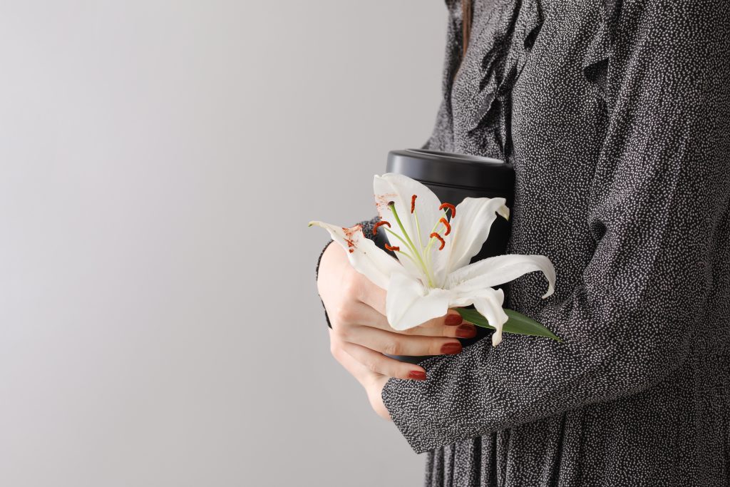 Woman with mortuary urn and lily flower on light background looking for a Probate Attorney in Tampa, FL