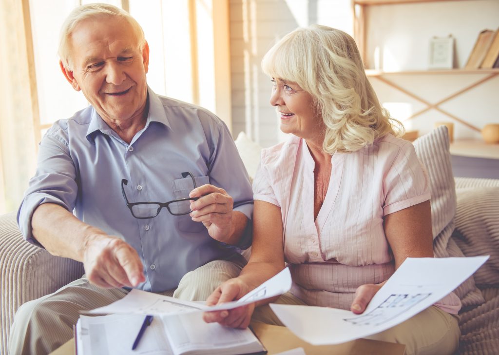 Handsome old man and beautiful woman are discussing house project and smiling while sitting on couch at home